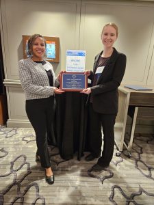 Two women posing together at an awards banquet and holding a placard award for the Neville A. Parker Award for achievement on a transportation-related project.